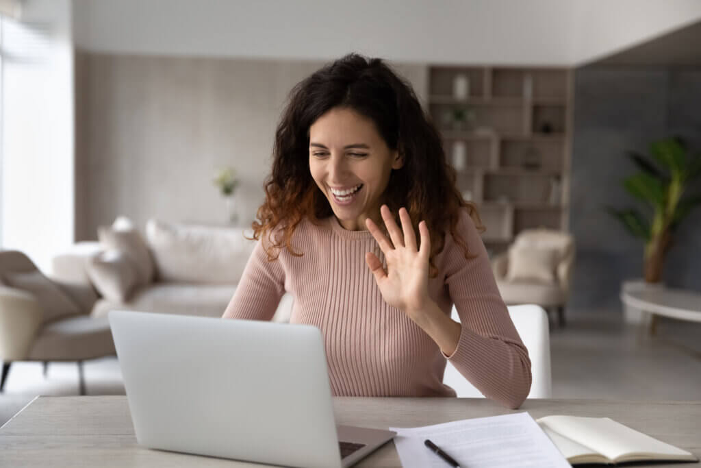 Smiling women waving hand at laptop webcam