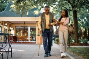 Smiling African American woman walking with her senior father, holding onto him to ensure he maintains balance during their walk together.