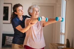 A senior woman is working out with a physical therapist, using dumbbells