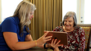Therapy staff providing holistic care by assisting a senior living resident with a telehealth call on a tablet.