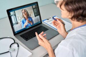 Female healthcare worker consulting older senior patient via a telehealth call visit using a laptop computer.