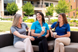 Three female therapists sitting together, talking and laughing, illustrating a healthy work-life balance