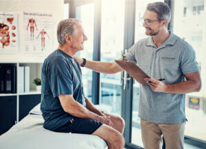 Physical therapist with a clipboard discussing longitudinal care with a senior resident in a healthcare setting