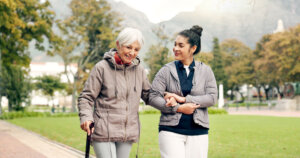 Senior woman with walker and caregiver walking in park, managing agitation in dementia through exercise.